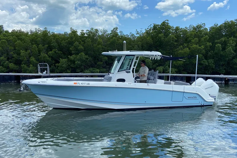 Slide: The Image of 2025 Boston Whaler 280 Outrage boat on water, with lush greenery in the background. - 11