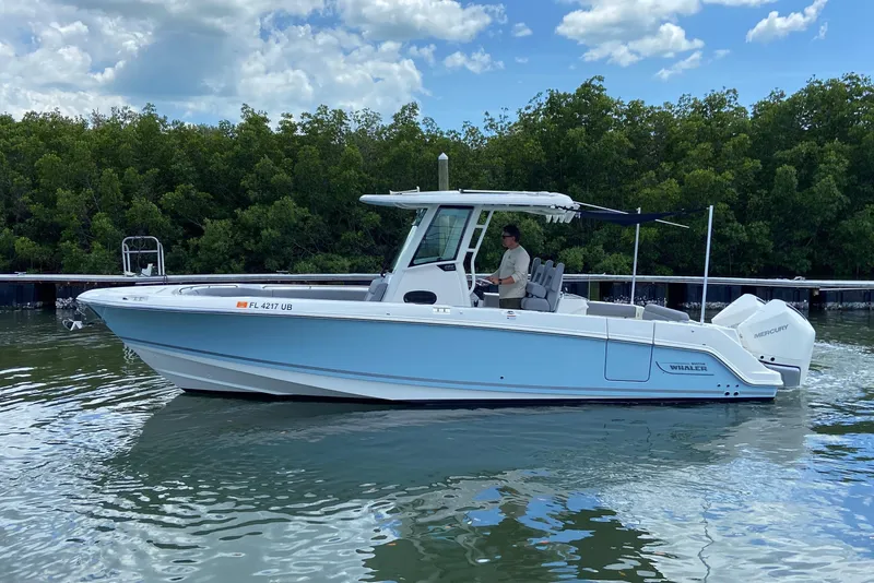 Slide: The Image of 2025 Boston Whaler 280 Outrage boat cruising on calm water near lush greenery. - 12