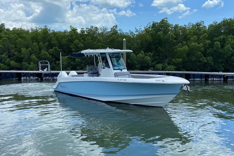 Slide: The Image of 2025 Boston Whaler 280 Outrage boat on calm water, surrounded by lush greenery. - 2