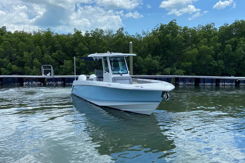 Slide: The Image of 2025 Boston Whaler 280 Outrage boat on calm water near a dock, surrounded by greenery. - 3