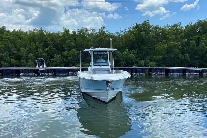 Slide: The Image of 2025 Boston Whaler 280 Outrage boat on calm water near a lush green shoreline. - 4