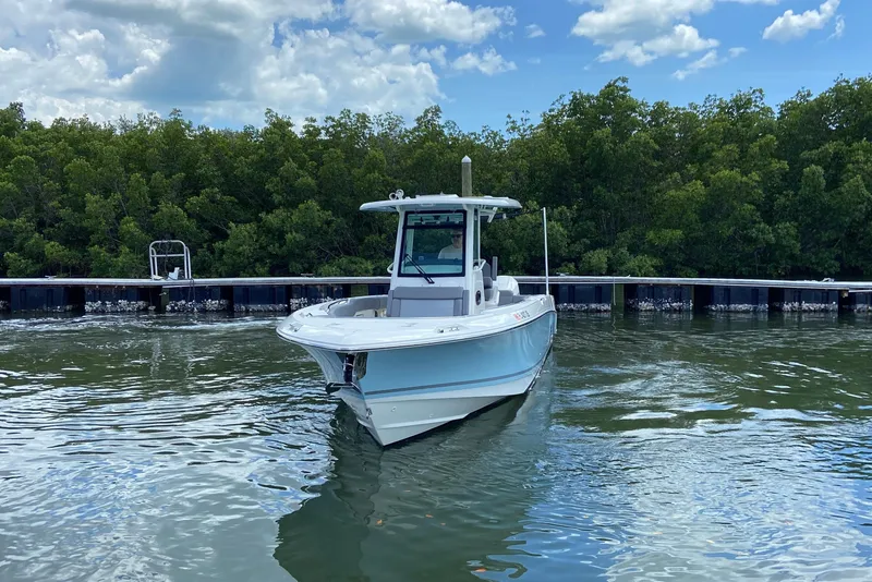 Slide: The Image of 2025 Boston Whaler 280 Outrage boat on calm water near a dock, surrounded by trees. - 5