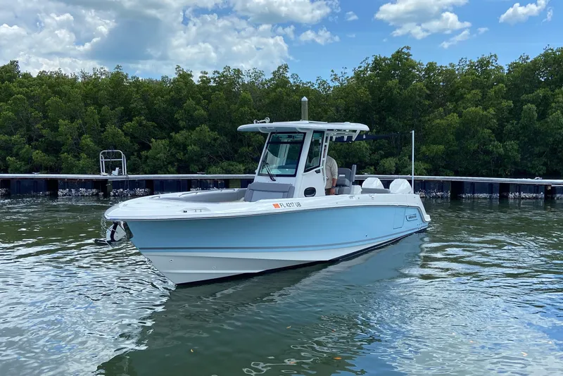 Slide: The Image of 2025 Boston Whaler 280 Outrage boat on calm water, surrounded by lush greenery. - 7