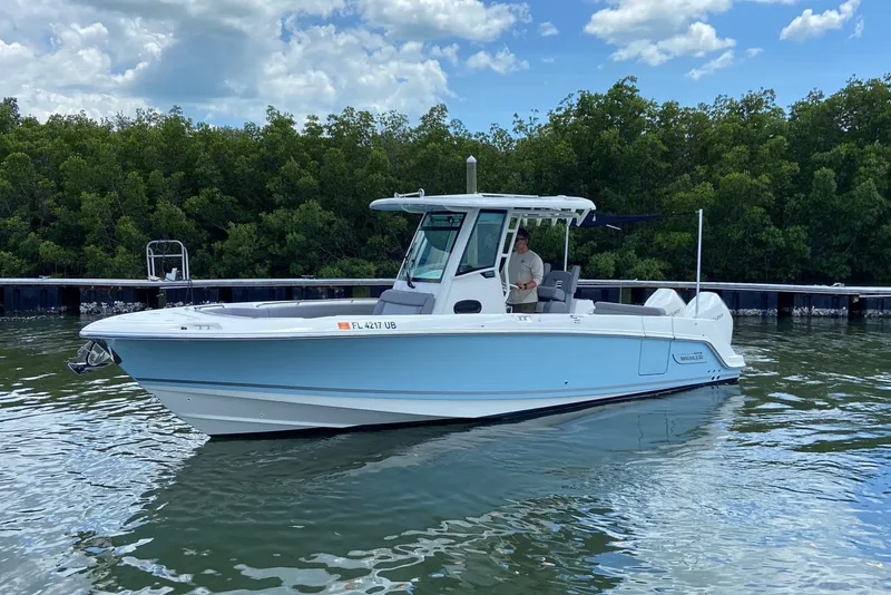 Slide: The Image of 2025 Boston Whaler 280 Outrage boat on calm water, surrounded by lush greenery. - 9