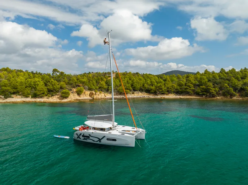 Slide: The Image of 2026 Excess 11 catamaran in turquoise waters near a wooded coastline. - 4