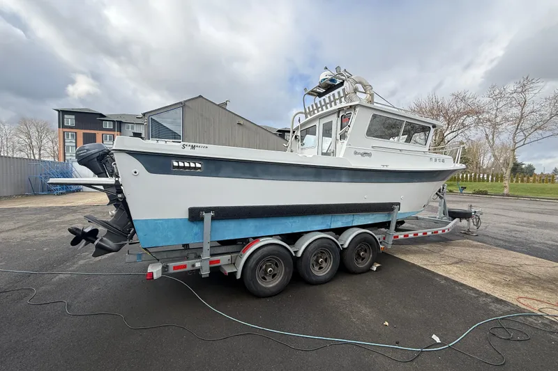 Slide: The Image of 1999 SeaSport Seamaster 2700 boat on a trailer, parked outdoors under cloudy skies. - 2