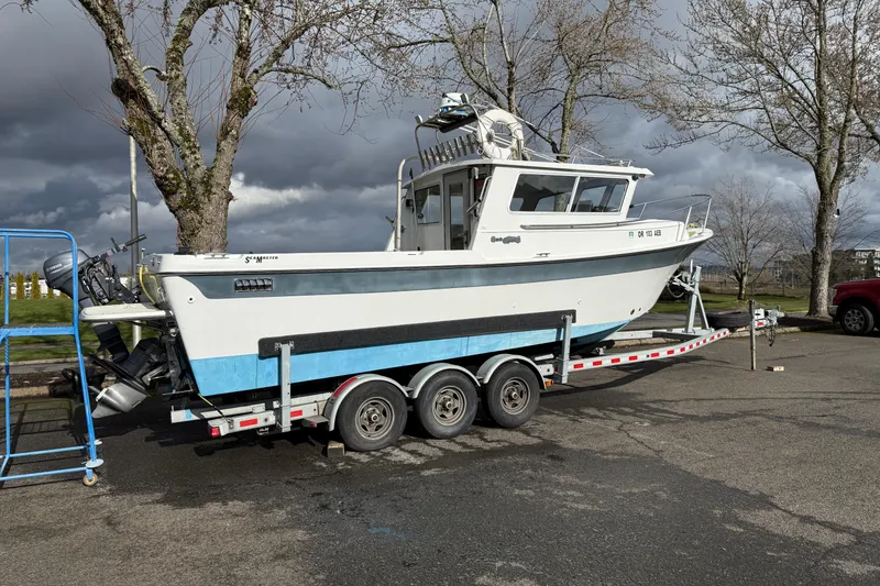 Slide: The Image of 1999 SeaSport Seamaster 2700 boat on trailer, parked near trees under cloudy sky. - 22