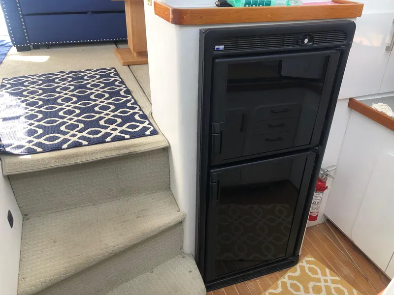 Slide: The Image of Interior of 1990 Trojan 40 Sport Fisherman with compact black fridge and carpeted stairs. - 7