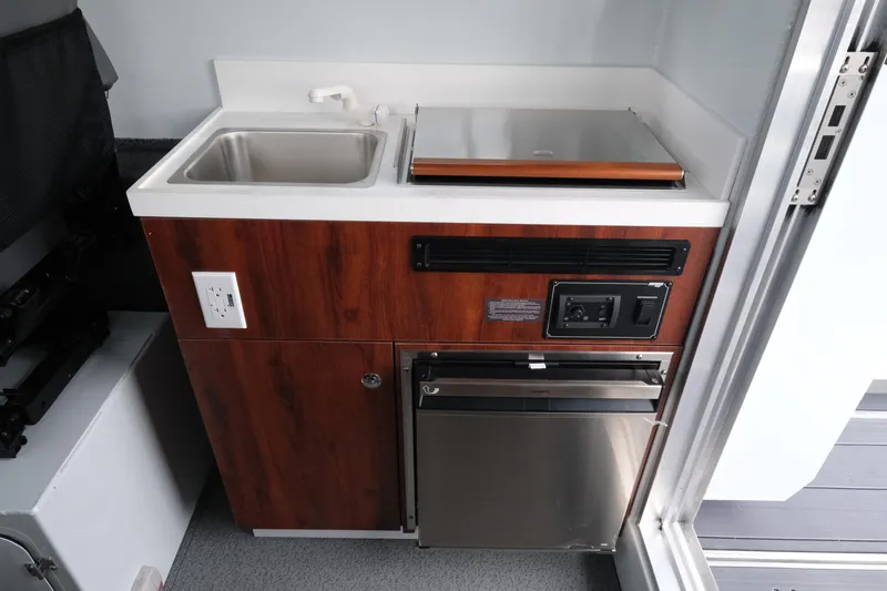 Slide: The Image of 2026 Hewescraft 270 Pacific Explorer kitchenette with sink, stove, and storage. - 15
