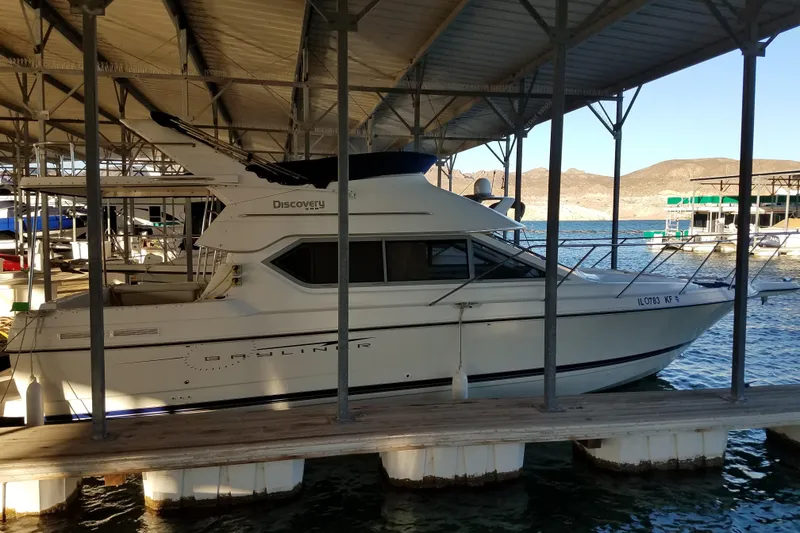 Slide: The Image of 2007 Bayliner Discovery 288 docked under a covered marina with scenic background. - 2