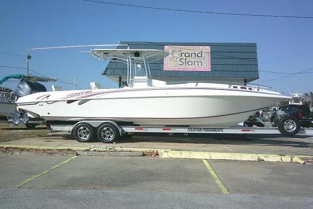 The Image of 1996 Fountain 31 Center Console boat on trailer, parked near a building. - 1