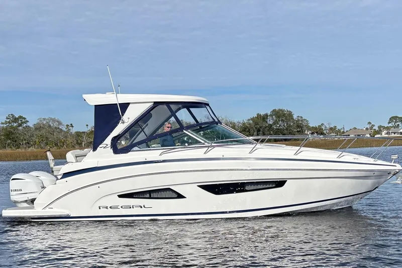 The Image of 2021 Regal 33 XO boat cruising on a calm waterway under a clear sky. - 0