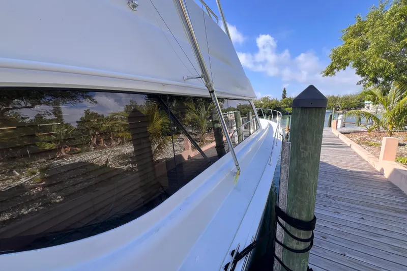 Slide: The Image of 2001 Hatteras 65 Convertible yacht docked beside a wooden pier, surrounded by lush greenery. - 20