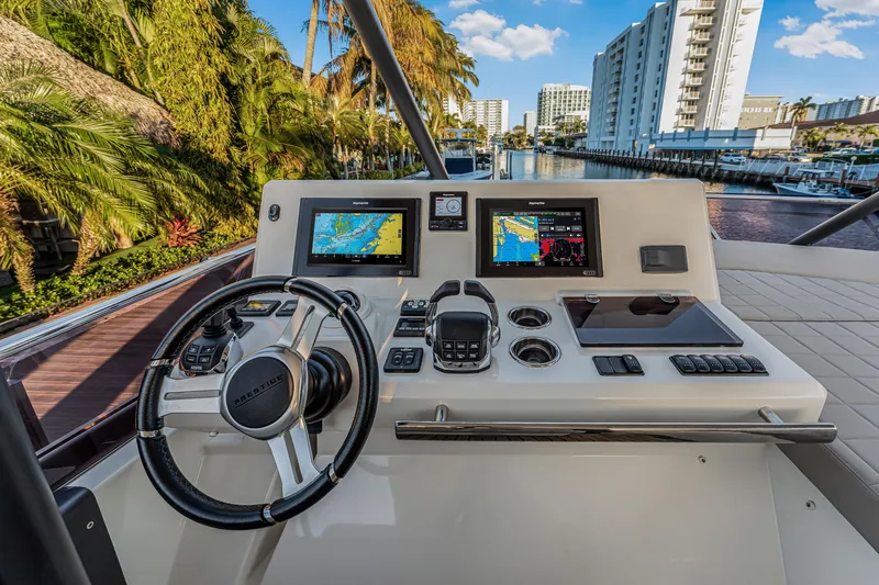 Slide: The Image of Prestige 520 yacht helm with navigation screens, steering wheel, and cityscape view, 2018 model. - 55