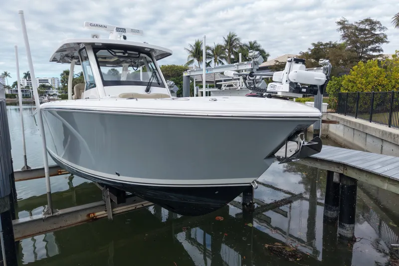 Slide: The Image of 2020 Pursuit S 328 Sport boat docked on a lift, surrounded by water and palm trees. - 2