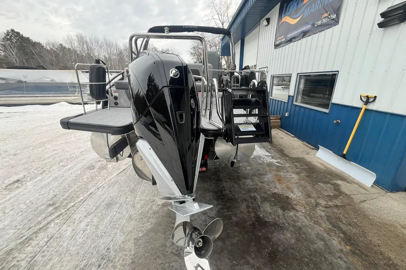 Slide: The Image of 2025 Harris Solstice 230 boat with powerful outboard motor, parked near a blue building. - 3