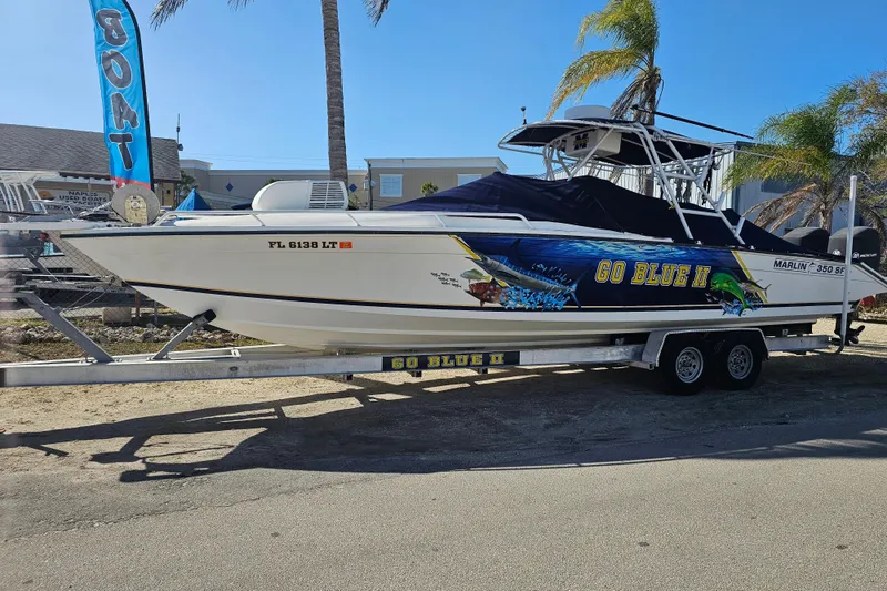 The Image of 1993 Marlin 350 Sportfish boat on trailer, vibrant "Go Blue II" graphics, palm trees in background. - 0