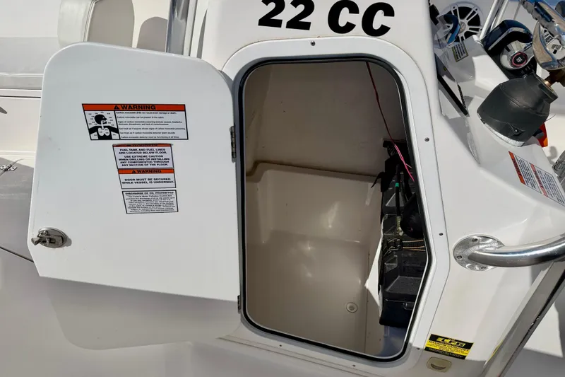 Slide: The Image of 2023 Aquasport 2200 Center Console storage compartment with open door and warning labels. - 28