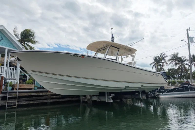 Slide: The Image of 2015 Cobia 344 Center Console boat docked near palm trees and waterfront house. - 1