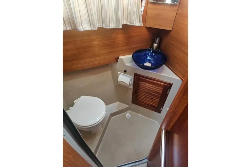 Slide: The Image of 2017 Ranger Tugs R-27 boat bathroom with toilet, blue sink, and wooden accents. - 11
