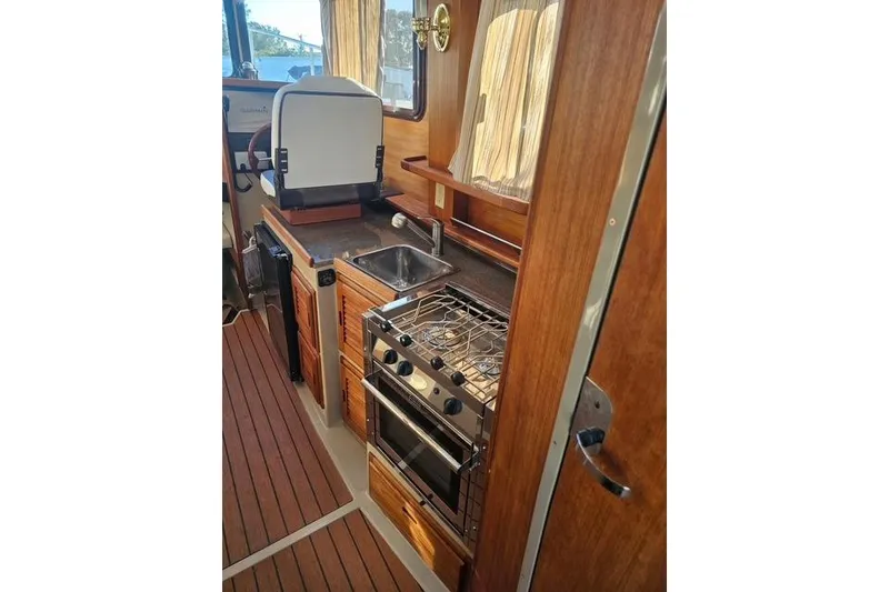 Slide: The Image of 2017 Ranger Tugs R-27 interior kitchen with stove, sink, and wooden cabinetry. - 12