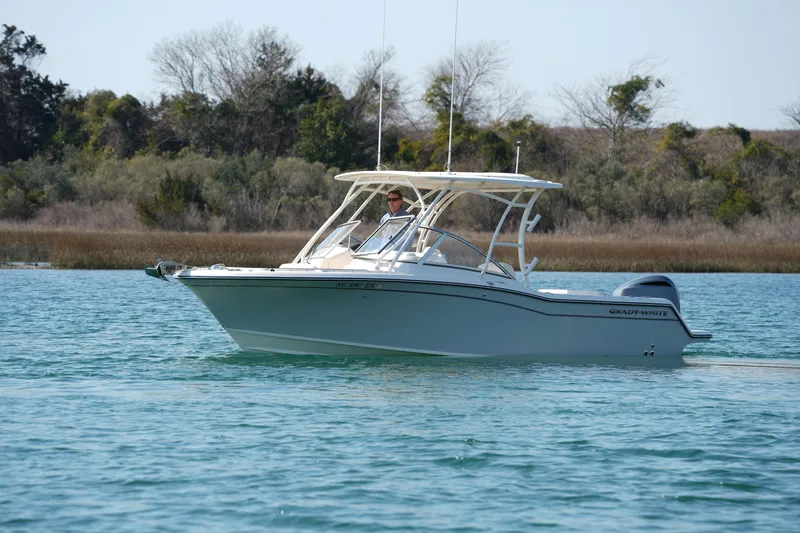 Slide: The Image of 2020 Grady-White Freedom 235 boat cruising on calm water near a wooded shoreline. - 2