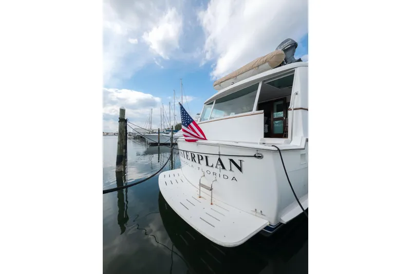 Slide: The Image of 1975 Hatteras 58 Long Range Cruiser docked with American flag, under cloudy sky. - 2