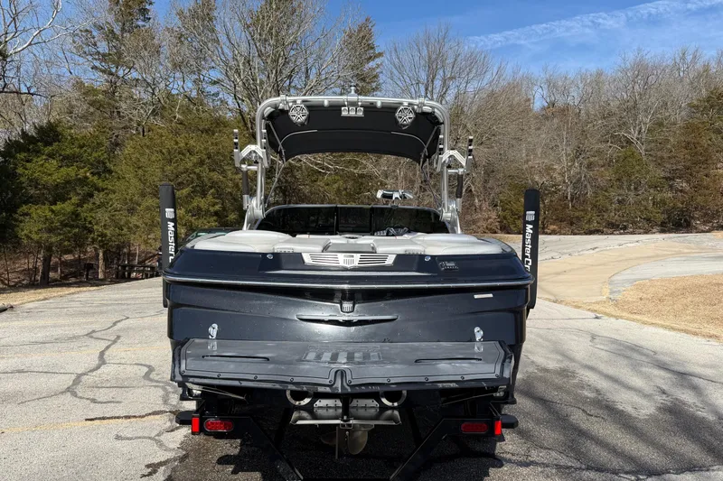 Slide: The Image of 2014 MasterCraft X30 boat, rear view, parked on a paved area with trees in background. - 4