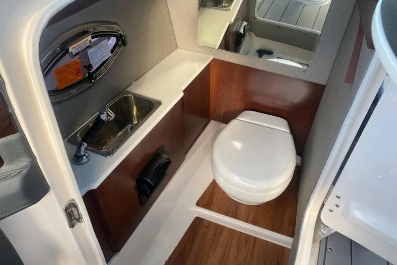 Slide: The Image of 2021 Chaparral 26 Surf boat interior with sink and toilet, featuring wood accents. - 11