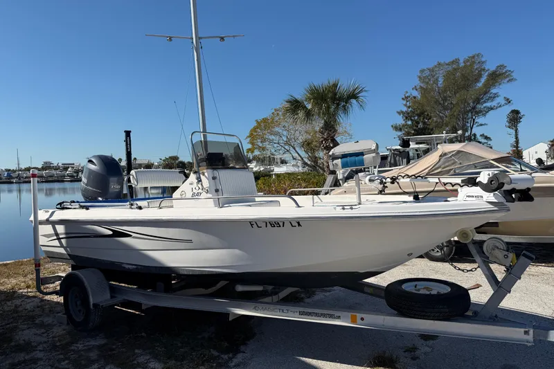 Slide: The Image of 2002 Cobia 191 Bay boat on trailer, parked near waterfront under clear blue sky. - 2