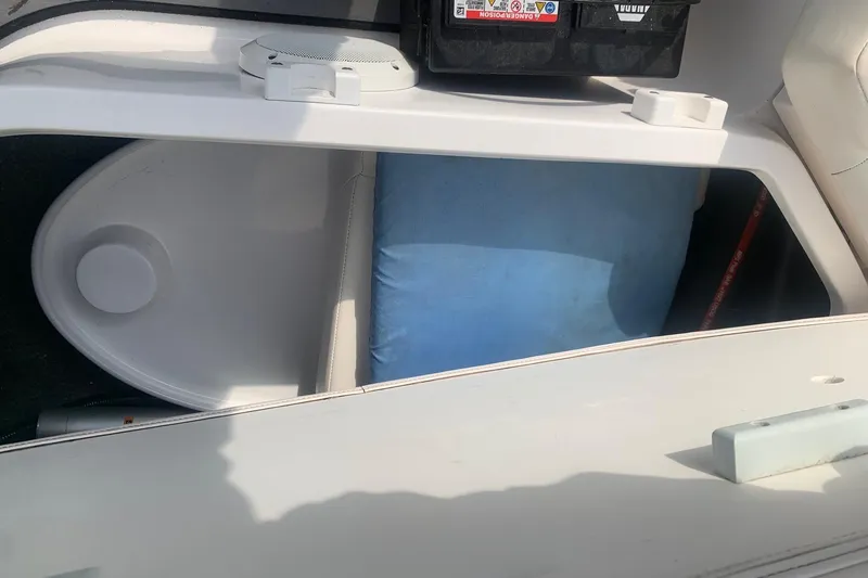 Slide: The Image of Storage compartment in a 2004 Yamaha AR230 boat, featuring a battery and blue cushion. - 24