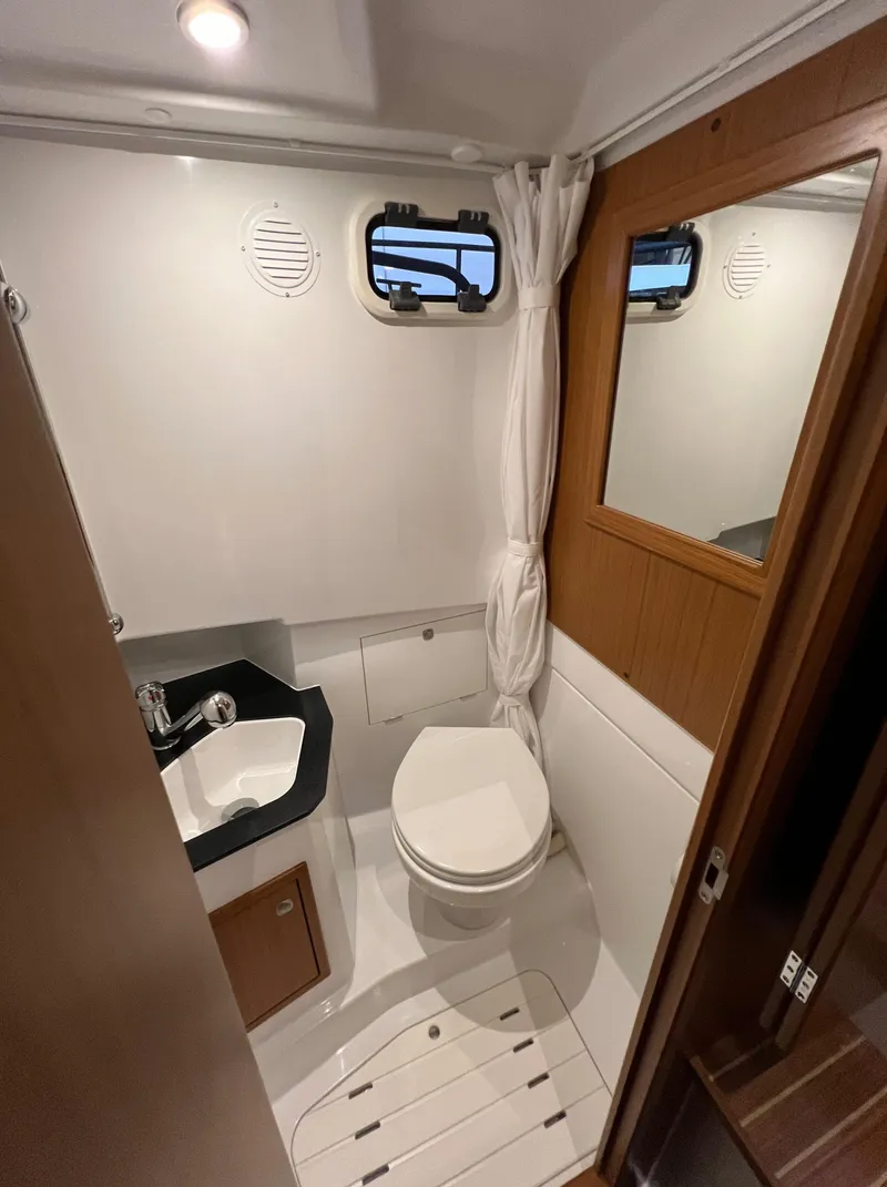 Slide: The Image of 2024 Sargo 28 boat bathroom with sink, toilet, mirror, and porthole windows. - 22
