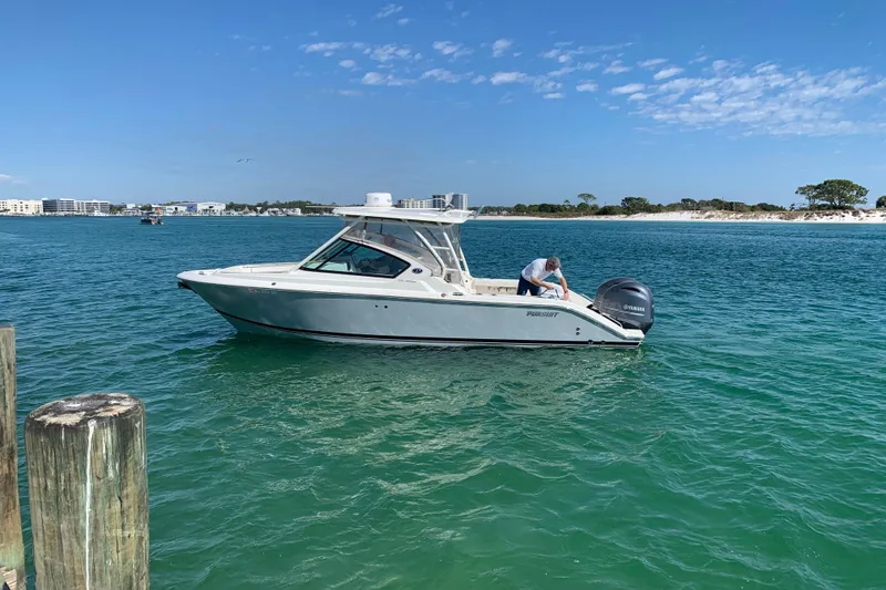The Image of 2023 Pursuit DC 266 Dual Console boat on clear blue water near a sandy shoreline. - 1