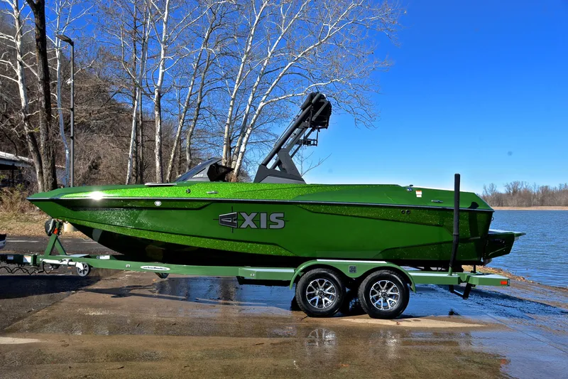 Slide: The Image of 2022 Axis A22 green boat on trailer by lake, clear blue sky. - 11