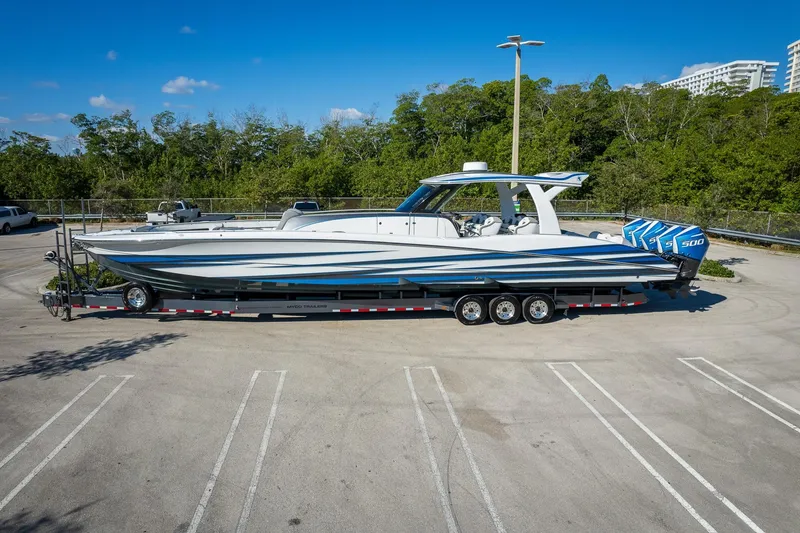Slide: The Image of 2023 MTI 50v boat on trailer in parking lot, surrounded by trees and clear sky. - 64