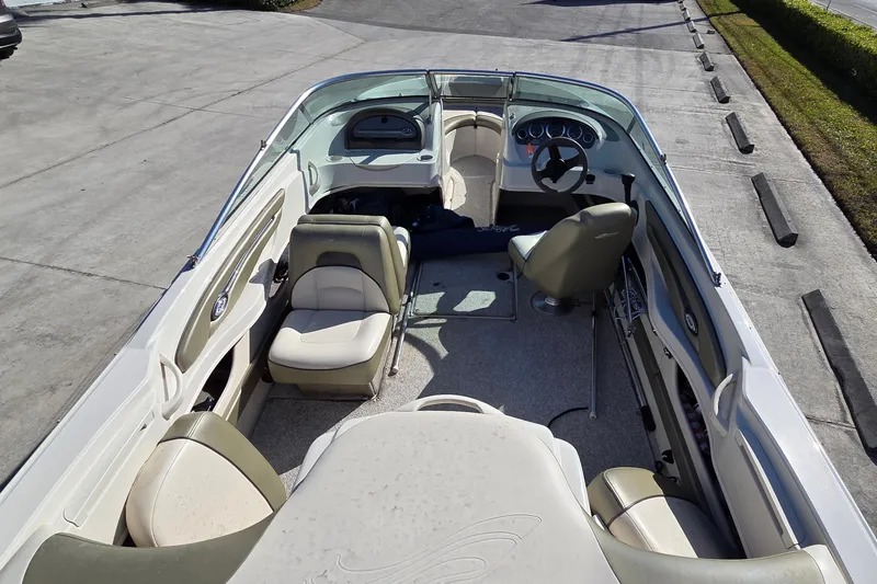 Slide: The Image of 2004 Sea Ray 200 Sport boat interior with seating and steering wheel, parked on concrete. - 4