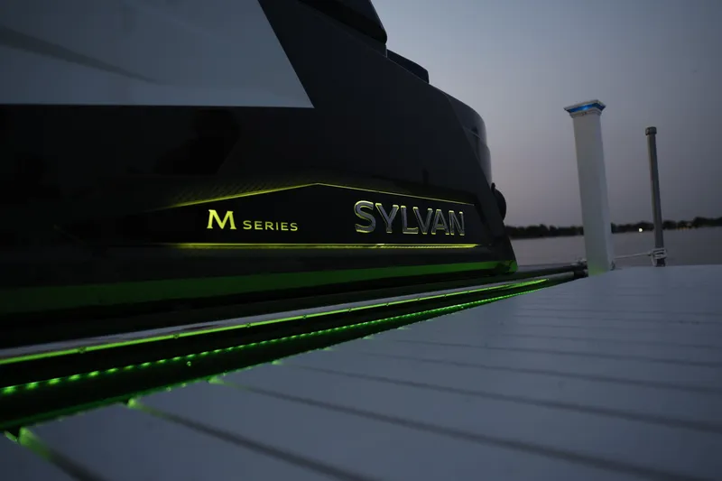 Slide: The Image of 2025 Sylvan M5 CLZ DC boat with illuminated branding at dusk. - 18