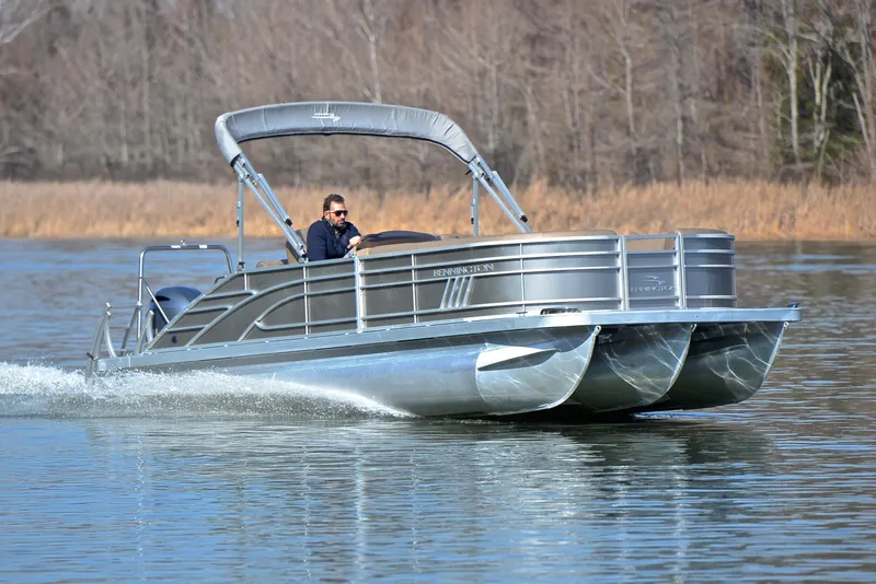 The Image of 2023 Bennington L23 pontoon boat cruising on a calm lake. - 1