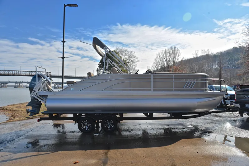 Slide: The Image of 2023 Bennington L23 pontoon boat on trailer by riverside, under clear sky. - 15