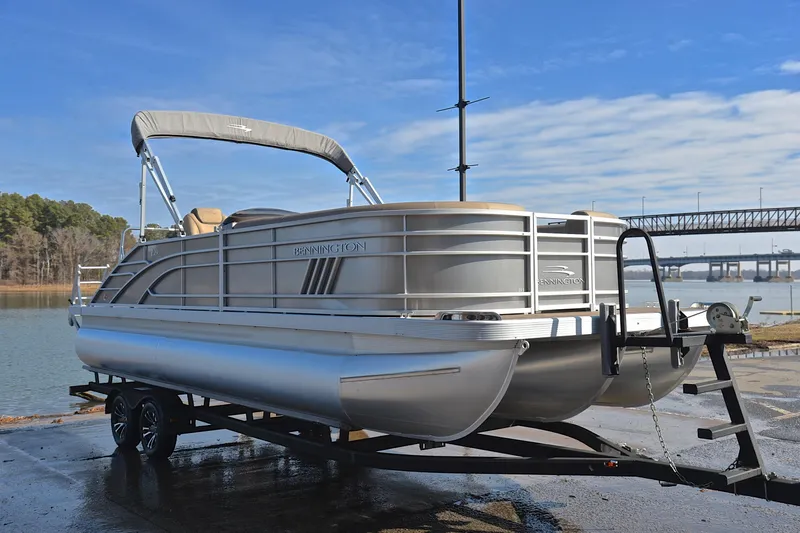 Slide: The Image of 2023 Bennington L23 pontoon boat on trailer by a lake with bridge in background. - 16