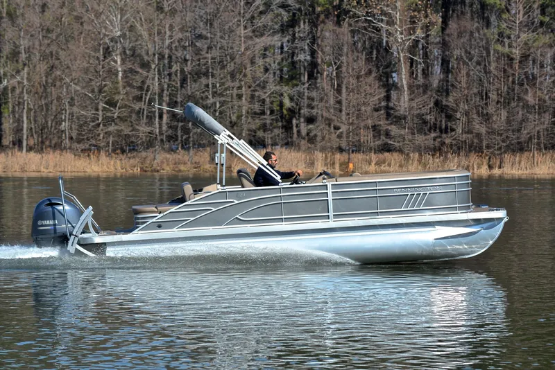 Slide: The Image of 2023 Bennington L23 pontoon boat cruising on a calm lake. - 3