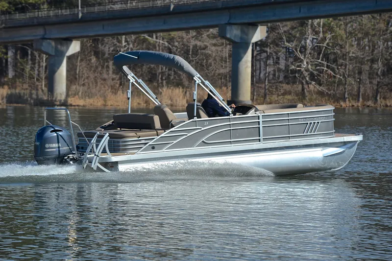 Slide: The Image of 2023 Bennington L23 pontoon boat cruising on a calm lake under a bridge. - 5