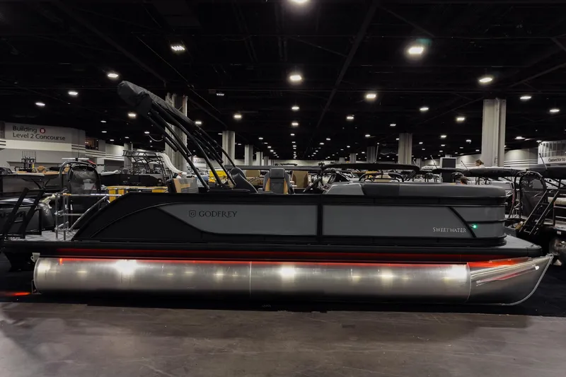 The Image of 2026 Godfrey Sweetwater 22' Tritoon boat displayed indoors at a showroom. - 2