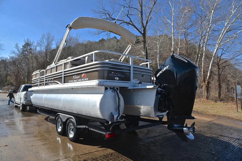 Slide: The Image of 2023 Sun Tracker SportFish 22 XP3 pontoon boat on trailer, parked near a wooded area. - 12