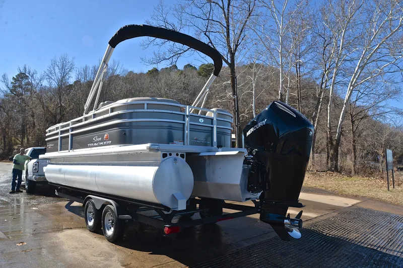 Slide: The Image of 2024 Sun Tracker Party Barge 22 XP3 pontoon boat on trailer, parked near trees. - 13