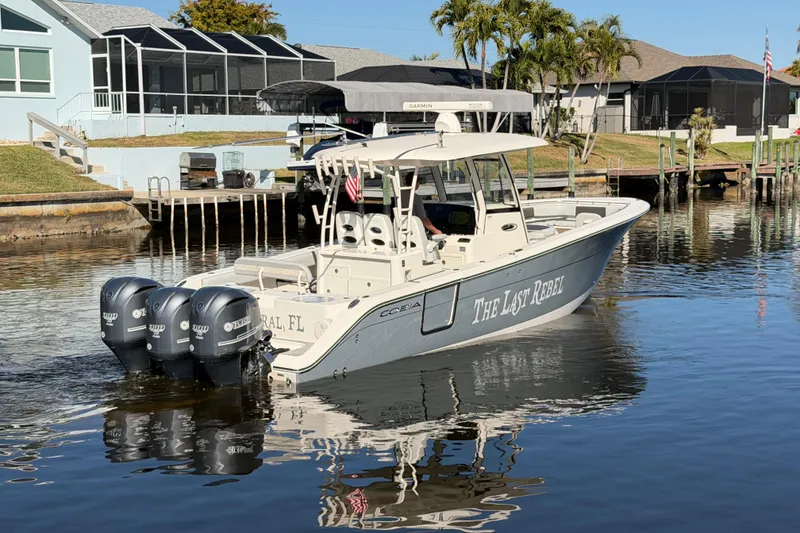 Slide: The Image of 2016 Cobia 344 Center Console boat docked on calm water, featuring triple Yamaha outboard engines. - 2