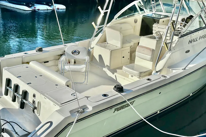 Slide: The Image of 2004 Pursuit 3070 Offshore boat with spacious deck and seating, docked on calm water. - 3