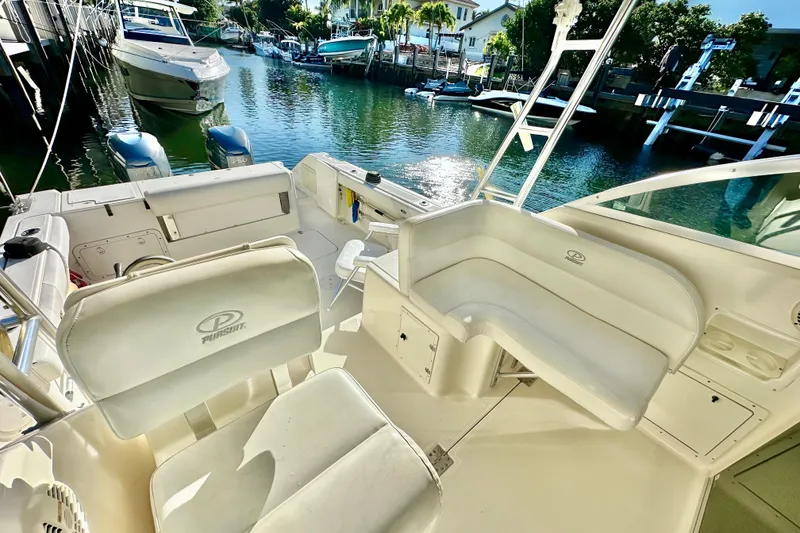 Slide: The Image of 2004 Pursuit 3070 Offshore boat interior with seating, docked by a scenic waterfront. - 53
