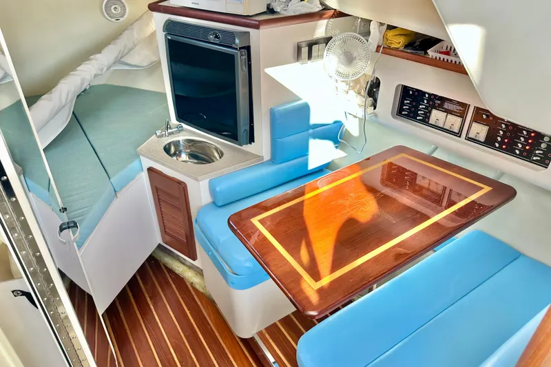 Slide: The Image of 2004 Pursuit 3070 Offshore cabin interior with blue seating, wooden table, and compact kitchenette. - 64