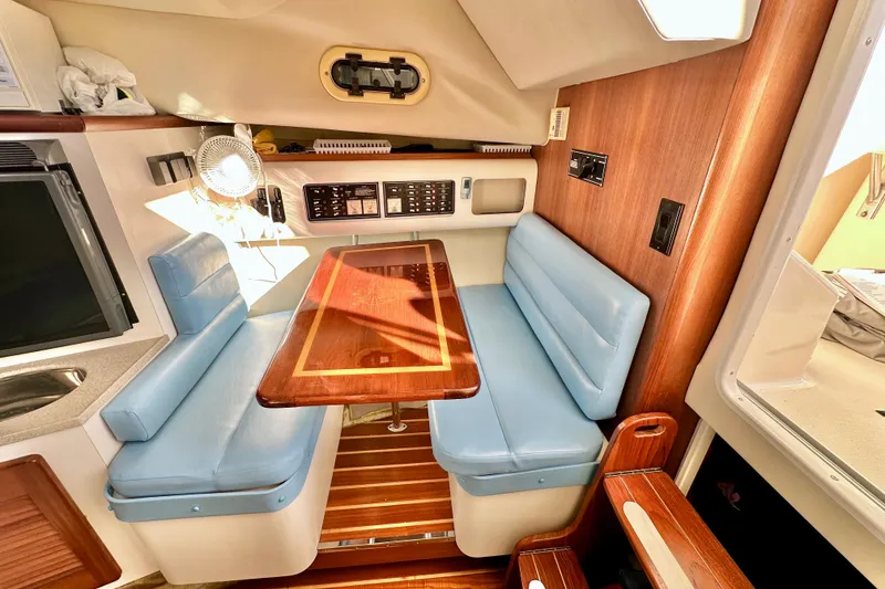 Slide: The Image of 2004 Pursuit 3070 Offshore cabin with blue seating and wooden table. - 65